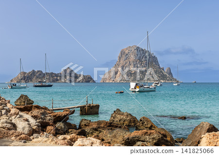 Es Vedra and Es Vedranell viewed by Cala d Hort with rustic jetty and anchored sailboats. Es Vedra and Es Vedranell viewed by Cala d Hort with rustic jetty and anchored sailboats. 141825066