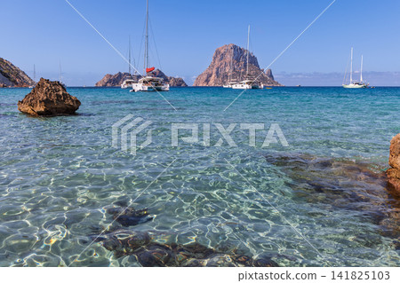Es Vedra and Es Vedranell across Cala d Hort bay with clear shallows and catamarans. Es Vedra and Es Vedranell across Cala d Hort bay with clear shallows and catamarans. 141825103
