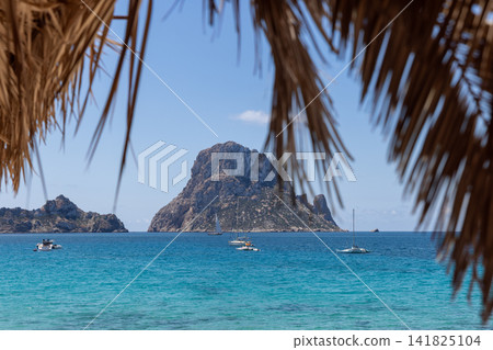 Es Vedra and Es Vedranell from the Cala d Hort shore with turquoise sea and palm fronds. Es Vedra and Es Vedranell from the Cala d Hort shore with turquoise sea and palm fronds. 141825104