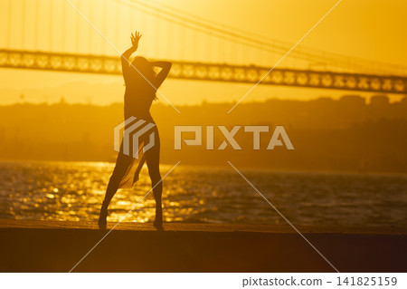 Dancer poses at sunset near bridge and water Dancer poses at sunset near bridge and water 141825159