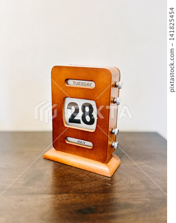 Vintage wooden perpetual desk calendar displaying Tuesday, July 28 on a dark tabletop against a neutral background Vintage wooden perpetual desk calendar displaying Tuesday, July 28 on a dark tabletop against a neutral background 141825454