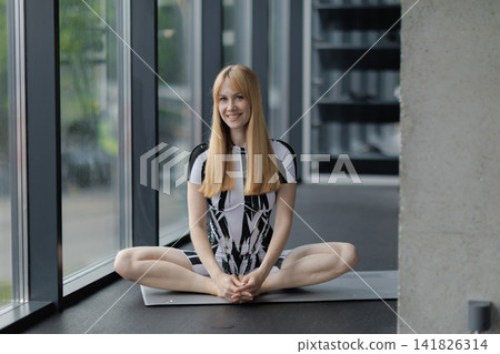Woman practicing yoga butterfly pose in modern gym Woman practicing yoga butterfly pose in modern gym 141826314