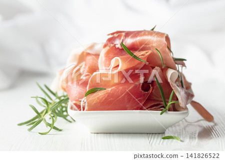 Prosciutto with rosemary on a white wooden table. 141826522