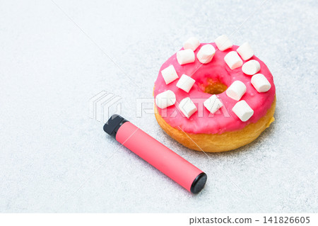 Colorful pink donut with marshmallows next to a vaping device on a light surface Colorful pink donut with marshmallows next to a vaping device on a light surface 141826605