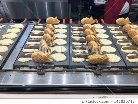 A scene from a shop kitchen where taiyaki (fish-shaped cakes) are being made using a taiyaki maker. A scene from a shop kitchen where taiyaki (fish-shaped cakes) are being made using a taiyaki maker. 141826712