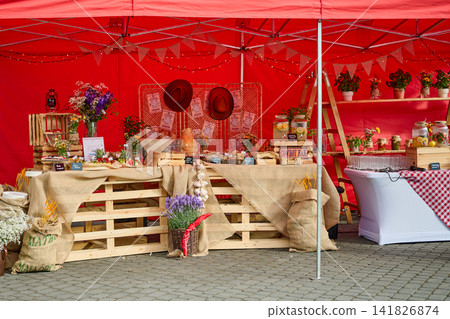 Warsaw, Poland, June 18, 2026 People gather around a market stall with a red tent, showcasing flowers and local food items in a lively outdoor space Warsaw, Poland, June 18, 2026 People gather around a market stall with a red tent, showcasing flowers and local food items in a lively outdoor space 141826874