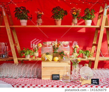 Warsaw, Poland, June 18, 2026 A busy stand features drink jars filled with lemon and herbs. There are glass cups ready for use. Colorful flowers decorate the background Warsaw, Poland, June 18, 2026 A busy stand features drink jars filled with lemon and herbs. There are glass cups ready for use. Colorful flowers decorate the background 141826879