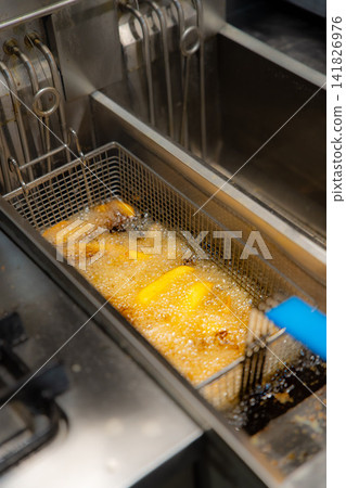 Basket of dices potatoes in the deep fryer of a restaurant kitchen. Overhead view Basket of dices potatoes in the deep fryer of a restaurant kitchen. Overhead view 141826976