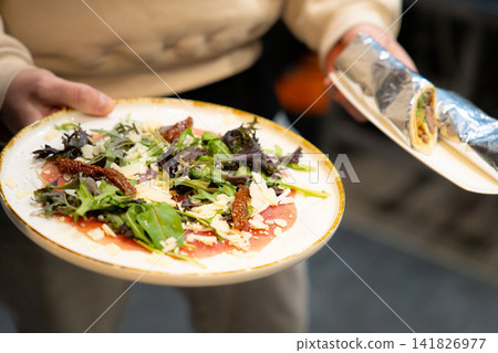 Beef Carpaccio cold appetizer with parmesan and arugula on a plate. Grey background. Top view. Beef Carpaccio cold appetizer with parmesan and arugula on a plate. Grey background. Top view. 141826977