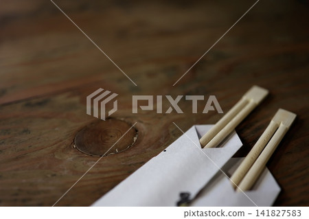 Two disposable chopsticks and a paper bag. Meal preparation. An image of a Japanese-style dining table placed on the table. Two disposable chopsticks and a paper bag. Meal preparation. An image of a Japanese-style dining table placed on the table. 141827583