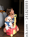 Girl sitting on floor with shih tzu dog in a plastic toy cart 141828893