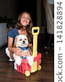 Girl sitting on floor with shih tzu dog in a plastic toy cart 141828894