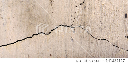 A deep crack in the texture of a cream-colored plastered concrete wall. 141829127