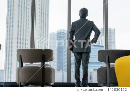 The back view of a senior businessman gazing at the city from the window of his office. The back view of a senior businessman gazing at the city from the window of his office. 141830112