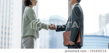 辦公室裡，一對資深生意夥伴（一男一女）握手。 141830114