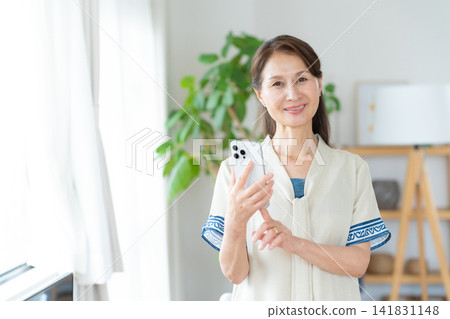 Senior woman looking at smartphone in living room Senior woman looking at smartphone in living room 141831148