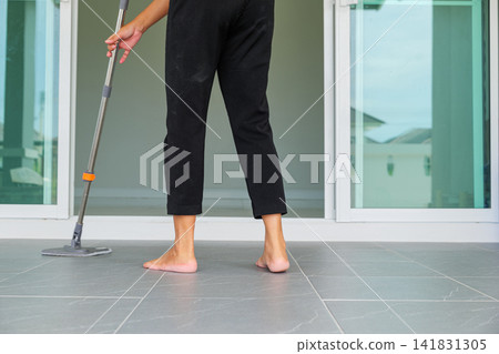 Asian woman mops the floor indoors, cleaning her outdoor front home with a mop and rag. Housewife maintaining a clean home. Represents the concept of professional housekeeping and house cleanup Asian woman mops the floor indoors, cleaning her outdoor front home with a mop and rag. Housewife maintaining a clean home. Represents the concept of professional housekeeping and house cleanup 141831305