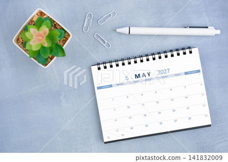 May 2027 desk calendar for 2026 and plant pot with pen on blue cement, Flat lay. May 2027 desk calendar for 2026 and plant pot with pen on blue cement, Flat lay. 141832009