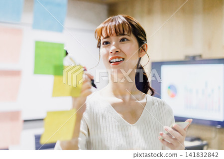 A woman having a meeting using a transparent board in a conference room A woman having a meeting using a transparent board in a conference room 141832842