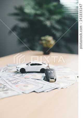 White toy car and car key on scattered dollar bills, symbolizing vehicle purchase payment, auto loan approval, car ownership, and transportation finance concept. White toy car and car key on scattered dollar bills, symbolizing vehicle purchase payment, auto loan approval, car ownership, and transportation finance concept. 141833147