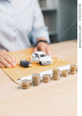 White toy car and car key presented over finance report with coin stacks nearby, representing auto loan approval, vehicle ownership transfer, and car insurance concept. White toy car and car key presented over finance report with coin stacks nearby, representing auto loan approval, vehicle ownership transfer, and car insurance concept. 141833148