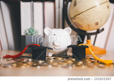Piggy bank with coins, two graduation caps, and a globe on a desk, representing education savings for multiple students, scholarship planning, study abroad, and global learning investment. Piggy bank with coins, two graduation caps, and a globe on a desk, representing education savings for multiple students, scholarship planning, study abroad, and global learning investment. 141833267