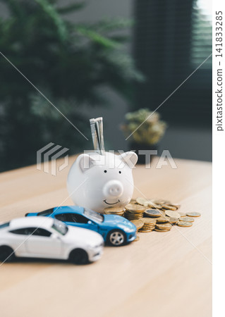 Piggy bank with cash, coins, and miniature cars on a desk, illustrating car savings, auto loan planning, vehicle insurance, personal finance, and transportation budget concept. Piggy bank with cash, coins, and miniature cars on a desk, illustrating car savings, auto loan planning, vehicle insurance, personal finance, and transportation budget concept. 141833285