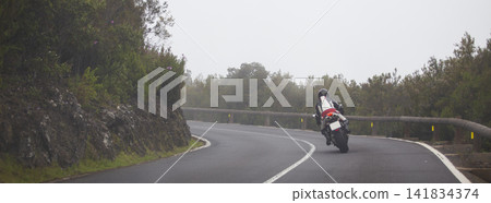 Motorcyclist riding on winding mountain road in fog, dynamic bike leaning with copy space Motorcyclist riding on winding mountain road in fog, dynamic bike leaning with copy space 141834374