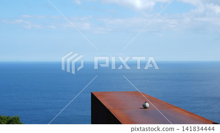 A round stone with a rope attached, placed on a rusty iron roof, and the sea. A round stone with a rope attached, placed on a rusty iron roof, and the sea. 141834444