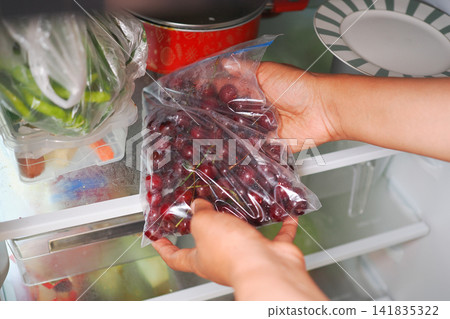 Person places bag of grapes in refrigerator Person places bag of grapes in refrigerator 141835322