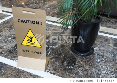 Caution sign placed on wet floor next to potted plant Caution sign placed on wet floor next to potted plant 141835357