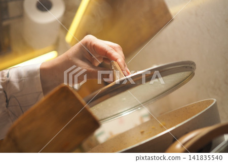 Hand lifting lid from pot in kitchen during cooking time Hand lifting lid from pot in kitchen during cooking time 141835540