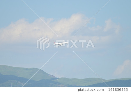 A jet plane soars into the sky with the majestic Aso mountain range as its backdrop. A jet plane soars into the sky with the majestic Aso mountain range as its backdrop. 141836333