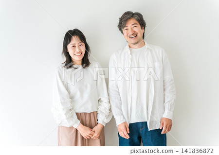 A smiling middle-aged couple, husband and wife, standing in front of a white background. A smiling middle-aged couple, husband and wife, standing in front of a white background. 141836872