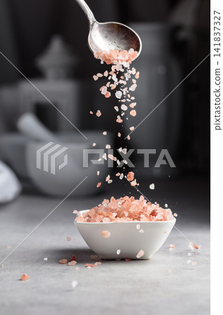 Pink salt in crystals is poured into a small white bowl. Pink salt in crystals is poured into a small white bowl. 141837327
