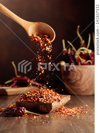 Chilli flakes are poured into a wooden dish. Chilli flakes are poured into a wooden dish. 141837331
