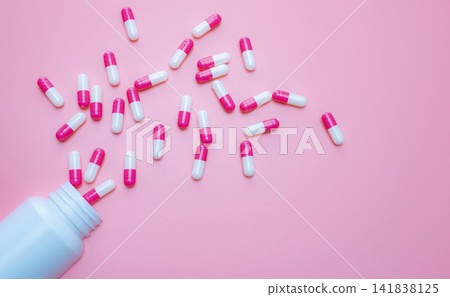 Pink-white capsules pill spilled out from plastic bottle container on pink background. Antibiotics drug resistance. Antimicrobial capsule pills. Pharmaceutical industry. Pill for happy love concept. Pink-white capsules pill spilled out from plastic bottle container on pink background. Antibiotics drug resistance. Antimicrobial capsule pills. Pharmaceutical industry. Pill for happy love concept. 141838125