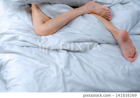 Woman barefoot on bed over white linen blanket and bed sheet in hotel or home bedroom. Sleep and relaxation. Lazy Sunday morning. Bare feet of woman chilling sleep on white comfort bed and duvet. Woman barefoot on bed over white linen blanket and bed sheet in hotel or home bedroom. Sleep and relaxation. Lazy Sunday morning. Bare feet of woman chilling sleep on white comfort bed and duvet. 141838169