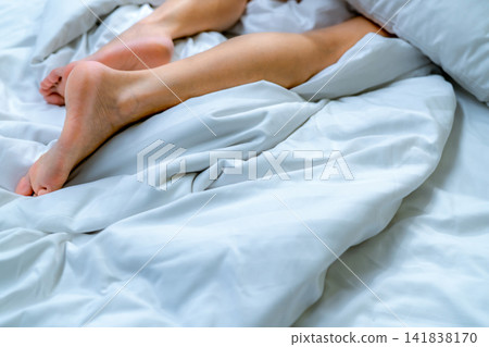 Woman barefoot on bed over white linen blanket and bed sheet in hotel or home bedroom. Sleep and relaxation. Lazy Sunday morning. Bare feet of woman chilling sleep on white comfort bed and duvet. Woman barefoot on bed over white linen blanket and bed sheet in hotel or home bedroom. Sleep and relaxation. Lazy Sunday morning. Bare feet of woman chilling sleep on white comfort bed and duvet. 141838170