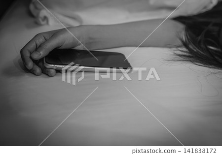 Asian woman sleeping in bed at home and hand holding mobile phone. Woman using smartphone in bedroom. Young woman addicted using smartphone. Texting on cellphone with tired until falling asleep. 141838172