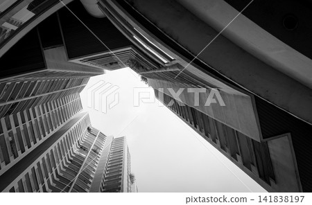 Black and white low angle view of modern high rise buildings reaching toward the sky. Geometric architecture, urban city development, contemporary real estate, business district and copy space. Black and white low angle view of modern high rise buildings reaching toward the sky. Geometric architecture, urban city development, contemporary real estate, business district and copy space. 141838197