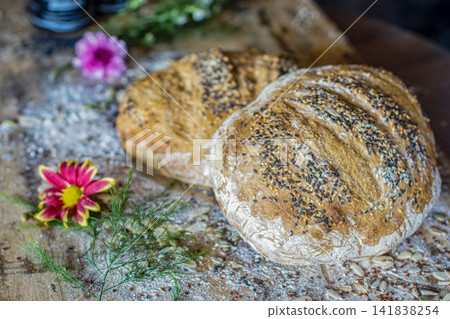 Homemade seeded artisan bread loaves on wooden table. Rustic bakery food and cozy lifestyle concept. Homemade seeded artisan bread loaves on wooden table. Rustic bakery food and cozy lifestyle concept. 141838254