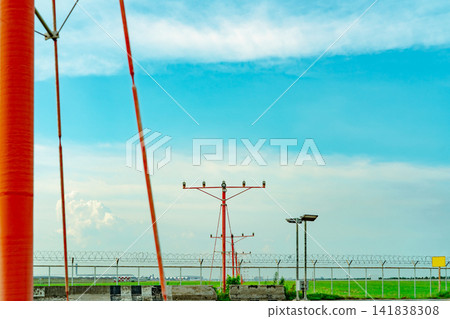 Airport runway approach lighting system with security fence and green grass field under blue sky. Aviation navigation infrastructure, aircraft landing guidance and modern airport safety technology. Airport runway approach lighting system with security fence and green grass field under blue sky. Aviation navigation infrastructure, aircraft landing guidance and modern airport safety technology. 141838308