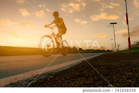 Motion blur sports man ride bicycles with speed motion on the road in the evening with sunset sky. Summer outdoor exercise for a healthy and happy life. Cyclist riding mountain bike on the bike lane. Motion blur sports man ride bicycles with speed motion on the road in the evening with sunset sky. Summer outdoor exercise for a healthy and happy life. Cyclist riding mountain bike on the bike lane. 141838339