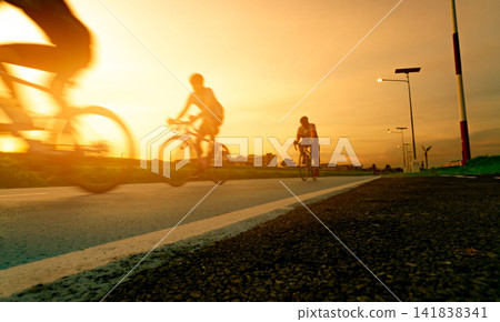 Blur photo sports man ride bicycles with speed motion on the road in the evening with sunset sky. Summer outdoor exercise for healthy and happy life. Cyclist riding mountain bike on bike lane. Team. Blur photo sports man ride bicycles with speed motion on the road in the evening with sunset sky. Summer outdoor exercise for healthy and happy life. Cyclist riding mountain bike on bike lane. Team. 141838341