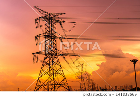 High voltage electric pylons and transmission lines with orange sunset sky and cityscape modern office building backgroud. Electricity pylons. Power and energy for city. High voltage grid tower. High voltage electric pylons and transmission lines with orange sunset sky and cityscape modern office building backgroud. Electricity pylons. Power and energy for city. High voltage grid tower. 141838669
