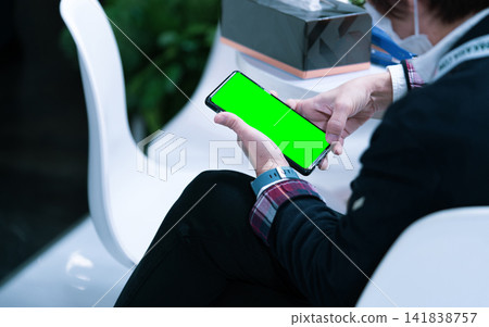 Person holding modern smartphone with green screen mockup while sitting indoors, perfect for mobile application, website presentation, user interface, digital marketing and technology concepts. Person holding modern smartphone with green screen mockup while sitting indoors, perfect for mobile application, website presentation, user interface, digital marketing and technology concepts. 141838757