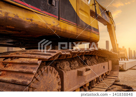 Closeup dirt track pad of backhoe. Digger parked at construction site. Bulldozer near concrete pole. Earth moving machine. Yellow digger with bucket. Earth moving machine. Excavation vehicle. Closeup dirt track pad of backhoe. Digger parked at construction site. Bulldozer near concrete pole. Earth moving machine. Yellow digger with bucket. Earth moving machine. Excavation vehicle. 141838848