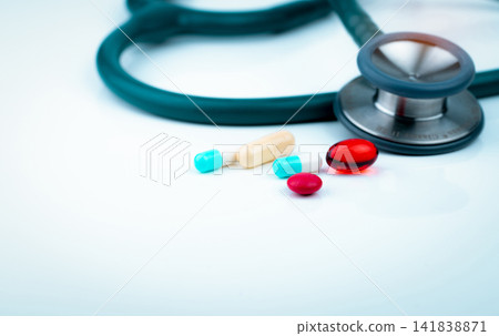 Stethoscope with blue-white capsule, red soft gel capsule pills, and red round tablets on doctor table or nurse desk. Medical healthcare and medicine background. Cardiology doctor diagnosis equipment. 141838871