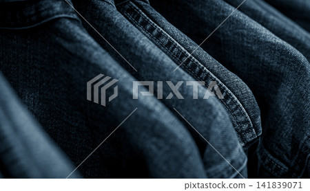 Selective focus on jacket jeans hanging on rack in clothes shop. Denim jeans with jeans pattern. Textile industry. Jeans fashion and shopping concept. Clothing concept. Denim jacket on rack for sale. Selective focus on jacket jeans hanging on rack in clothes shop. Denim jeans with jeans pattern. Textile industry. Jeans fashion and shopping concept. Clothing concept. Denim jacket on rack for sale. 141839071